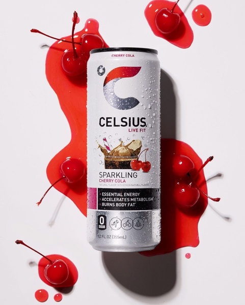 A top-down, high-key studio photograph of a cherry cola energy drink can surrounded by fresh cherries and organic red liquid splashes.